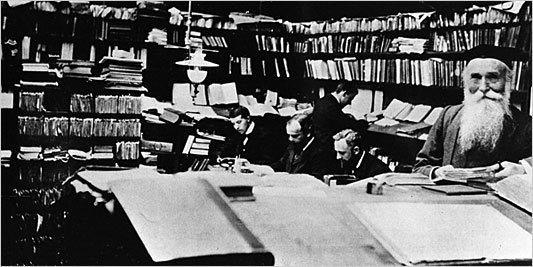 The OED team working in a book-filled room. James Augustus Henry Murray in the foreground; four of his staff working behind him.