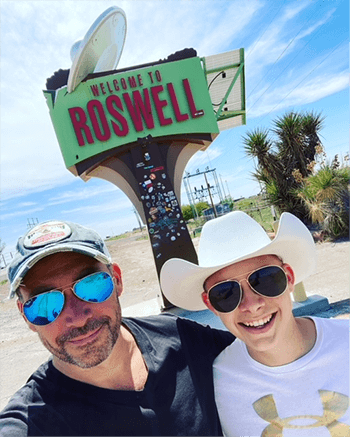 Robert Moran and his son, Asa, pose in front of a sign that reads, 'Welcome to Roswell.'