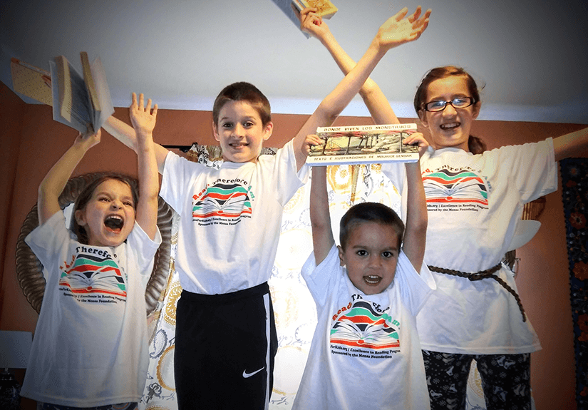 Four children wearing Excellence in Reading shirts celebrate their accomplishment.
