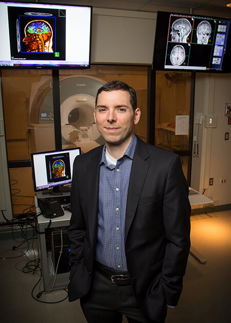 Portrait: Dr. Barbey stands in the lab, standing in front of an fMRI machine.