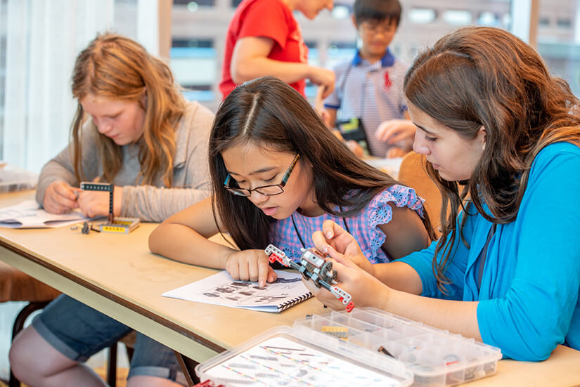 Several young girls work together to build a LEGO car